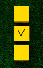 Three yellow cubes with a tick on one on grass. Concept of choosing a better option, creating checklists, elections and sports betting