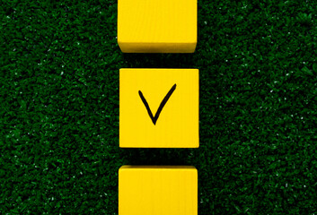 Three yellow cubes with a tick on one on grass. Concept of choosing a better option, creating...