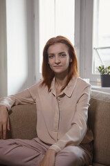 Caucasian young good looking woman with red hair sitting on the sofa in room and Woman looking at camera, smiling and laughing. Joy, warmth, happiness.