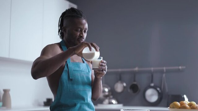 Sexy african fill glass with milk from bottle and drink standing on kitchen in blue back splash and posing for the camera. High quality footage.