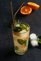 .Cold lemonade with orange and mint. Ice cubes on black background