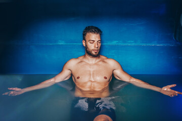 Handsome young bearded man floating in tank filled with dense salt water used in meditation, therapy, and alternative medicine.
