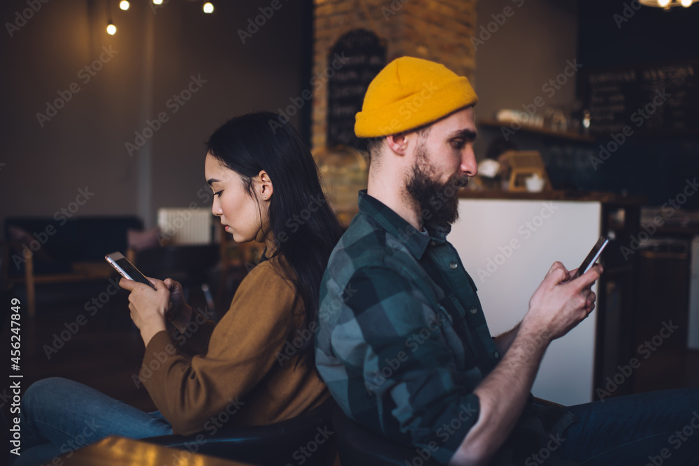 Poster side view of millennial hipster guys ignoring live communication sitting back against each other and