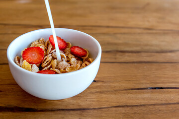 Pouring milk into cornflakes with strawberry. Breakfast with milk and cornflakes.
