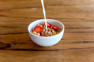 Pouring milk into cornflakes with strawberry. Breakfast with milk and cornflakes.