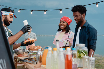 African young couple watching for the process of preparing hot dogs they having lunch on the beach outdoors