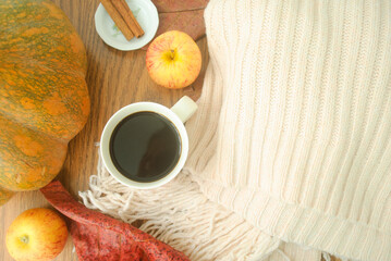 cup of coffee, pumpkin, cinnamon sticks, apples and a coat in a wood place