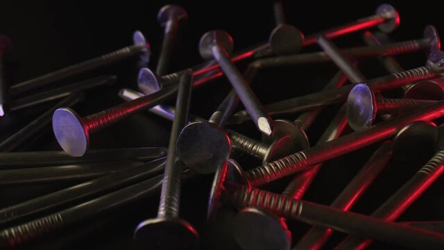 The camera moves slowly over a pile of nails with sharp rods. Metal, fasteners. A few nails are illuminated with red light on a dark background. High quality. 4k footage.
