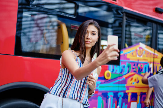 Youthful Asian female tourist making selfie pictures for creating travel content for web blog using front camera on modern mobile technology, charming hipster girl shooting influence video