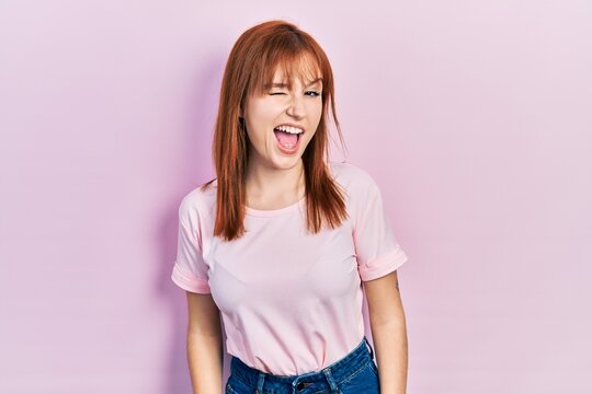 Redhead young woman wearing casual pink t shirt winking looking at the camera with sexy expression, cheerful and happy face.