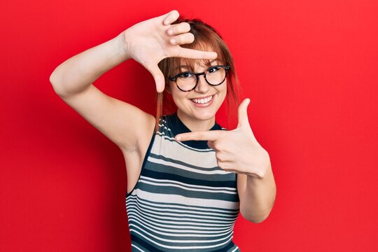 Redhead young woman wearing casual clothes and glasses smiling making frame with hands and fingers with happy face. creativity and photography concept.