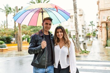 Young couple smiling happy holding umbrella standing at the city.