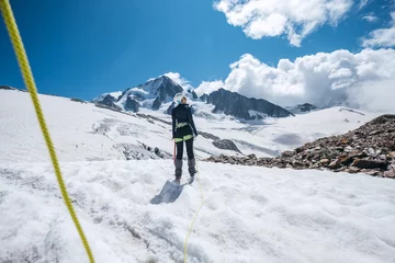 Cercles muraux Mont Blanc Young female Back view portrait Rope team member on acclimatization day dressed mountaineering clothes walking by snowy slopes in climbing harness and green dynamic rope on the close-up foreground.