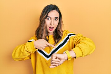 Young hispanic girl wearing casual clothes in hurry pointing to watch time, impatience, upset and angry for deadline delay - obrazy, fototapety, plakaty