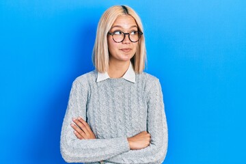 Beautiful blonde woman wearing glasses smiling looking to the side and staring away thinking.