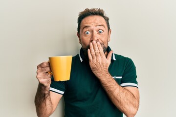 Middle age man drinking a cup of coffee covering mouth with hand, shocked and afraid for mistake....