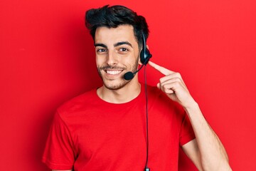 Young hispanic man wearing call center agent headset smiling happy pointing with hand and finger
