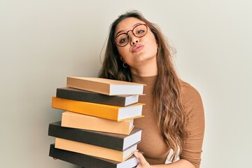 Young hispanic girl holding a pile of books looking at the camera blowing a kiss being lovely and sexy. love expression.