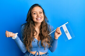 Young hispanic girl holding el salvador flag screaming proud, celebrating victory and success very...