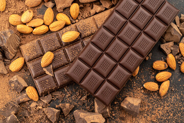 Cooking chocolate bars with almonds, desserts, handmade sweets. Composition of bars and pieces milk and dark chocolate, grated cocoa on black background top view. Confectionery craft on table