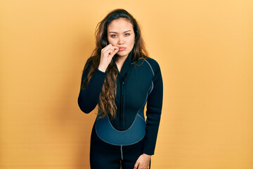 Young hispanic girl wearing diver neoprene uniform mouth and lips shut as zip with fingers. secret...