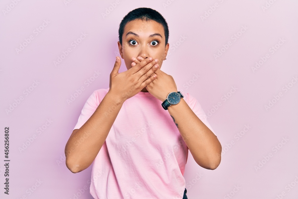 Wall mural Beautiful hispanic woman with short hair wearing casual pink t shirt shocked covering mouth with hands for mistake. secret concept.