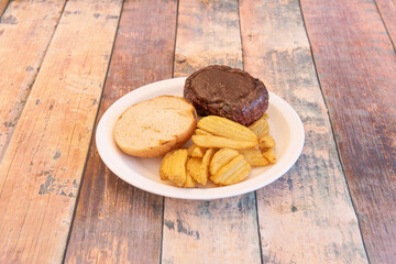 Piece of grilled beef with barbecue sauce on top inside hamburger bun garnished with wedge fries