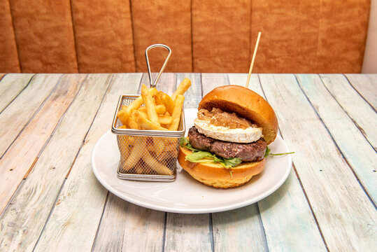 Beef burger with grilled brioche bread, goat cheese, stewed onion, arugula and fried potatoes in a metal basket