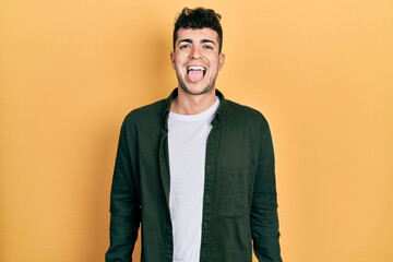 Young hispanic man wearing casual clothes sticking tongue out happy with funny expression. emotion concept.