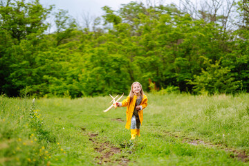 Little girl in a yellow cloak and rubber boots  launches a toy airplane into the sky. Childhood, active rest, lifestyle concept.