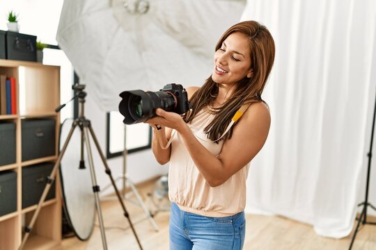 Young hispanic photographer woman smiling happy using camera at photo studio.