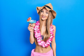 Young blonde girl wearing bikini and hawaiian lei drinking cocktail looking positive and happy...