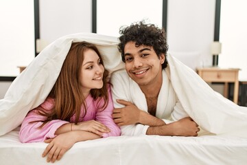 Young couple covering with bedsheet lying on the bed at bedroom.