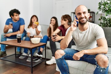 Group of young friends having party sitting on the sofa at home. Man smiling happy talking on the smartphone at home.