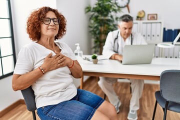 Senior woman sitting at doctor appointment smiling with hands on chest with closed eyes and grateful gesture on face. health concept.