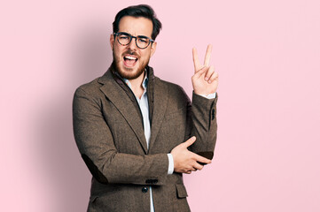 Young hispanic man wearing business jacket and glasses smiling with happy face winking at the...