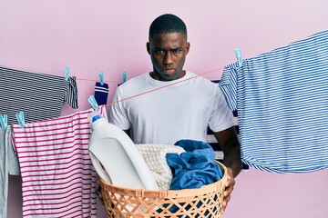 Young african american man holding laundry basket skeptic and nervous, frowning upset because of...