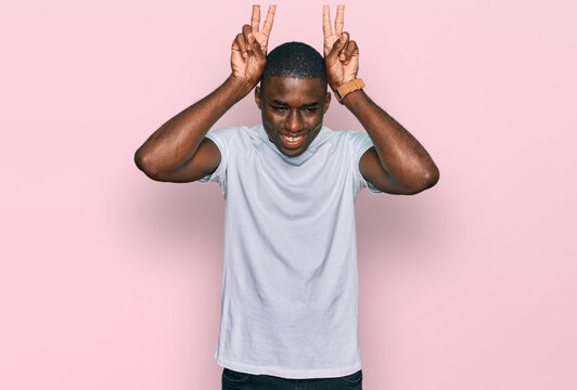 Young african american man wearing casual white t shirt posing funny and crazy with fingers on head as bunny ears, smiling cheerful