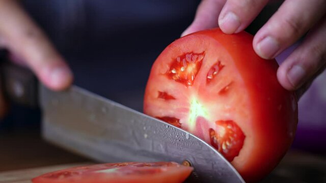 close up of hands slicing fresh tomato on cutting board with knife