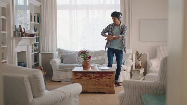 happy young man dancing at home celebrating success listening to music wearing headphones having fun dance in living room on weekend 