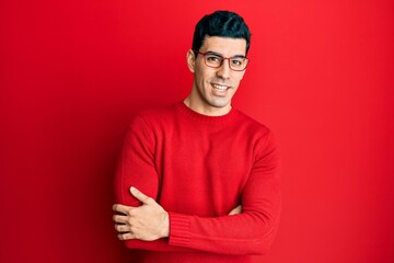 Handsome hispanic man wearing casual clothes and glasses happy face smiling with crossed arms looking at the camera. positive person.