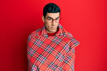 Handsome hispanic man wrapped in a red warm red blanket skeptic and nervous, frowning upset because of problem. negative person.
