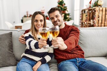 Young hispanic couple smiling happy toasting with champagne sitting on the sofa at home.