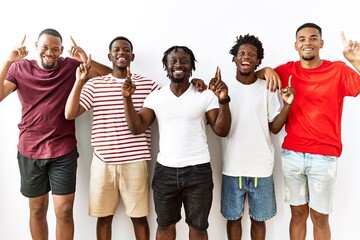 Young african group of friends standing together over isolated background smiling amazed and surprised and pointing up with fingers and raised arms.