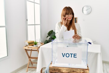 Hispanic business woman voting putting envelop in ballot box mouth and lips shut as zip with...