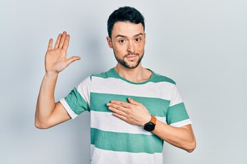Young hispanic man wearing casual clothes swearing with hand on chest and open palm, making a...