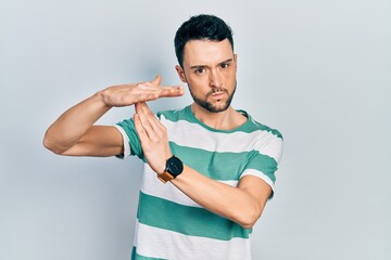 Young hispanic man wearing casual clothes doing time out gesture with hands, frustrated and serious...