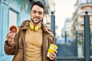 Young hispanic man having breakfast using headphones at the city.