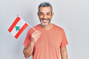 Handsome middle age man with grey hair holding lebanon flag looking positive and happy standing and...