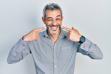 Handsome middle age man with grey hair pointing mouth with fingers winking looking at the camera...